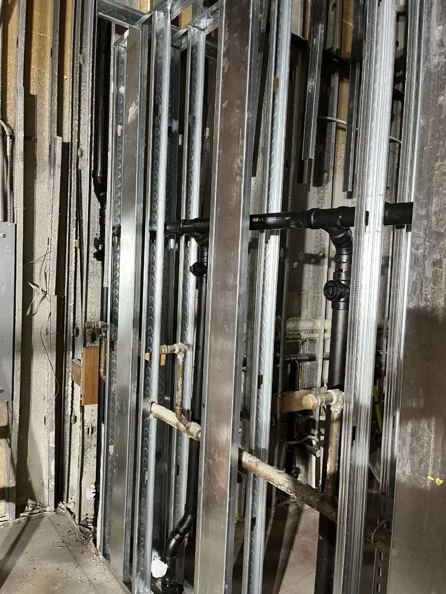 Charred wall framing and blackened studs after a fire, with exposed pipes and debris.