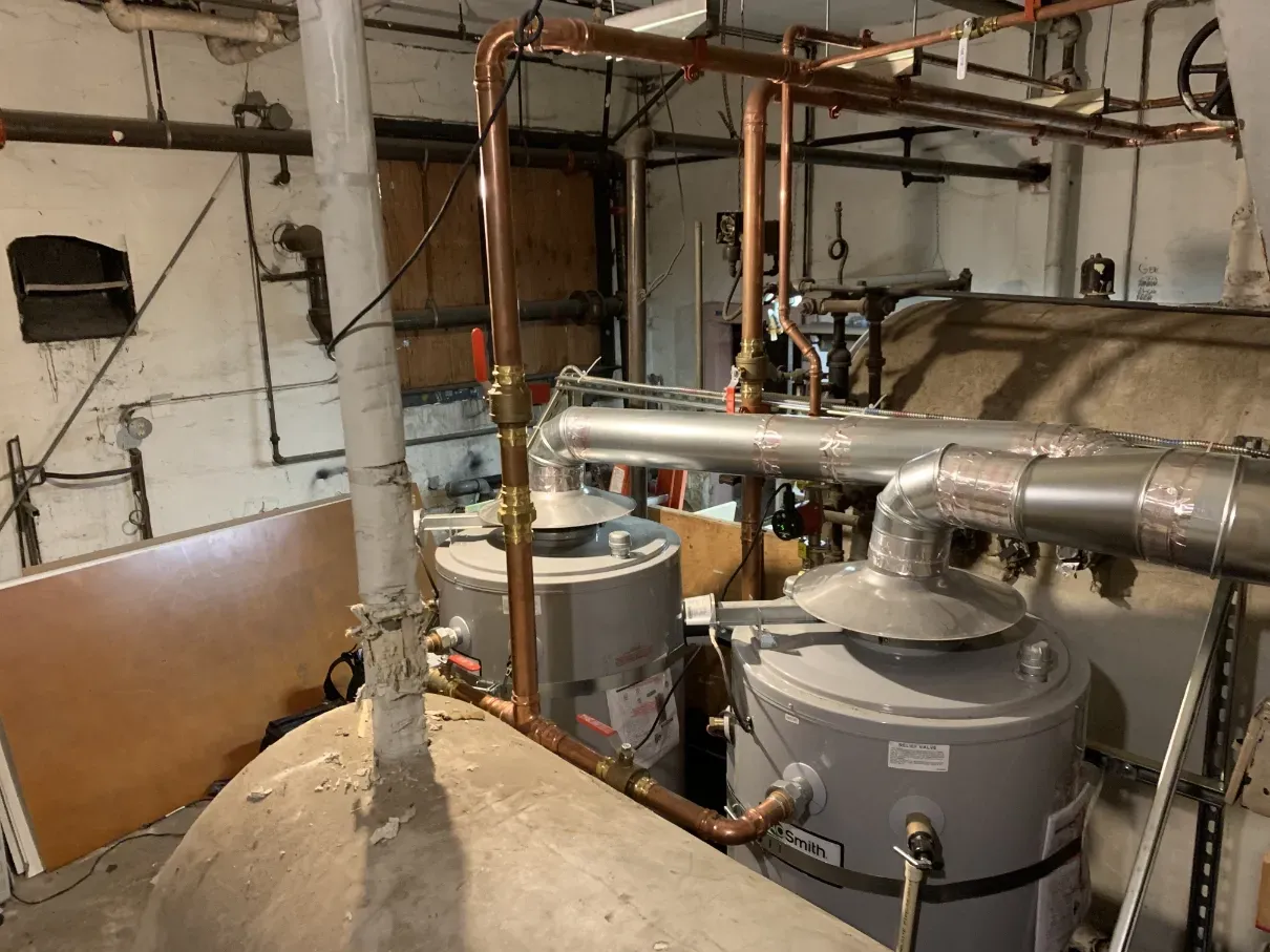 Basement mechanical room with boiler tanks, pipes, and HVAC equipment in a utility area