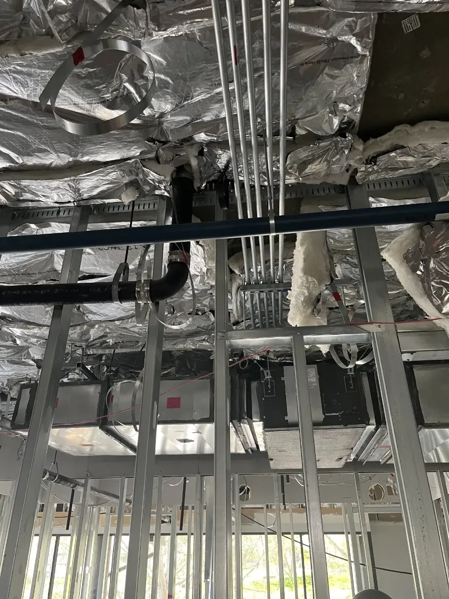 Exposed ceiling with foil insulation, hanging pipes, and metal framing in a construction site