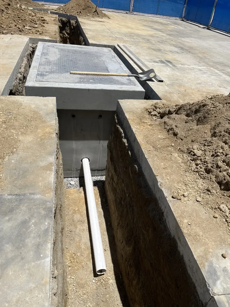 Construction trench with concrete utility box and open manhole cover beside a dirt excavation