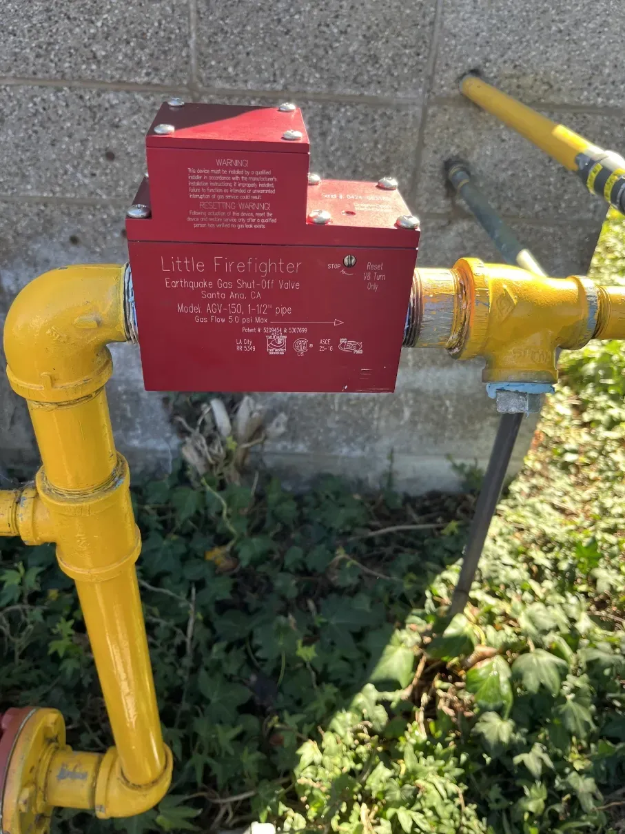 Yellow gas pipe with red utility box and valve outdoors beside grass and sidewalk
