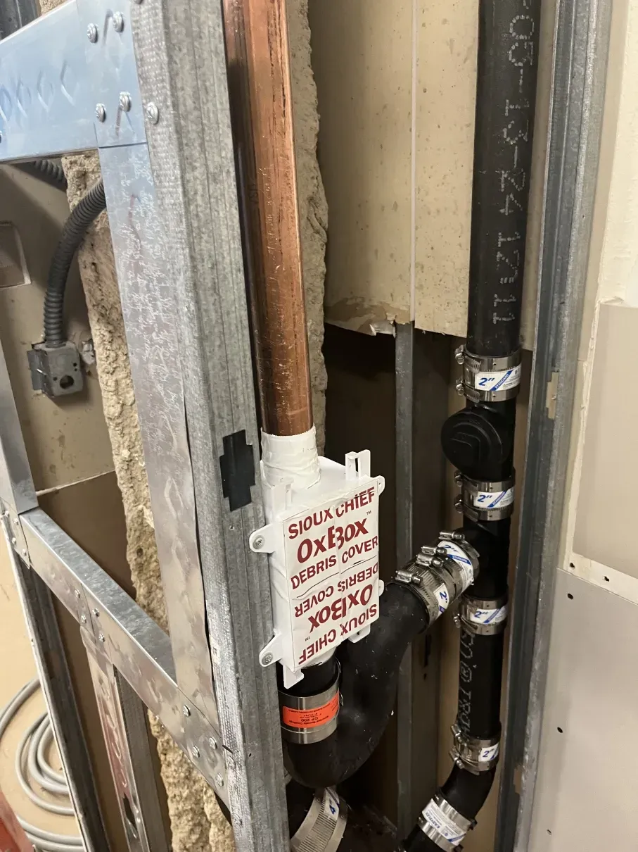 Plumbing pipes and a valve with a red warning tag inside a wall opening