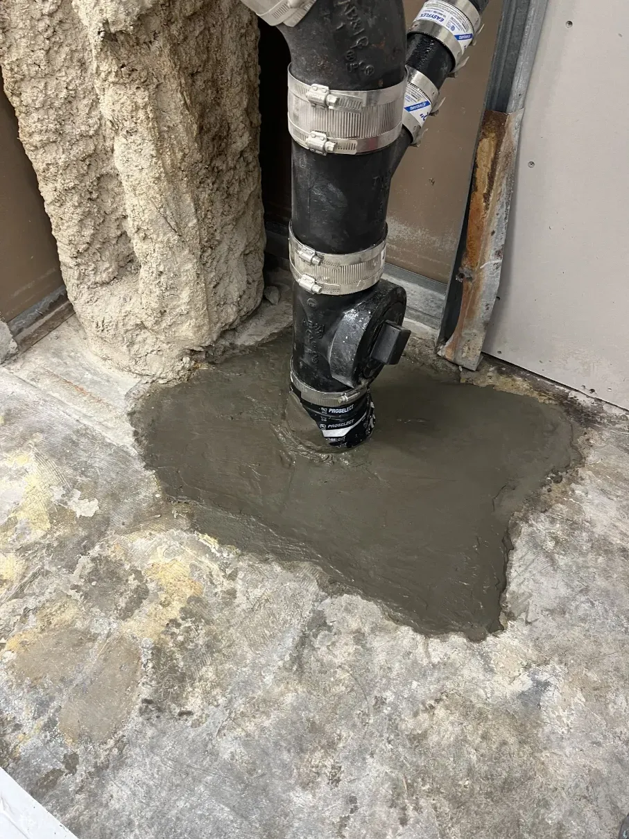 Exposed black pipe set in fresh gray concrete near a wall and rough stone surface