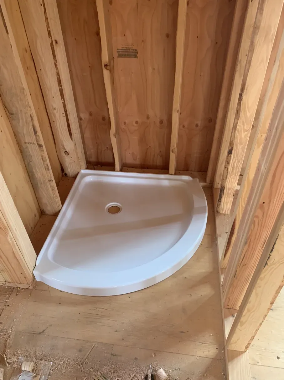 White shower pan in a unfinished wooden bathroom frame with exposed studs and subflooring