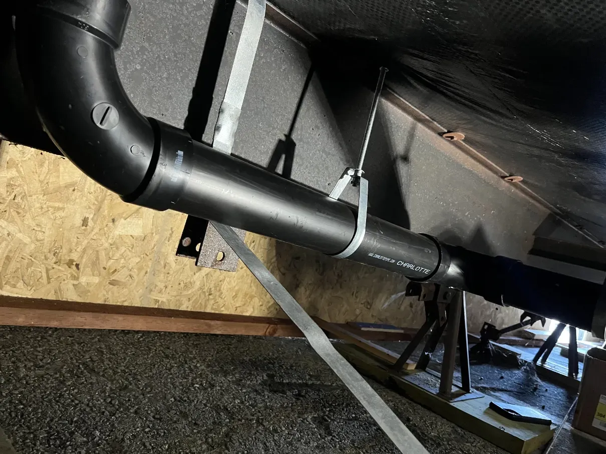 Black plumbing pipes under a floor with insulation and gravel around them