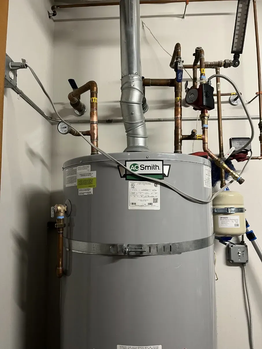 Large gray water heater with pipes, valves, and wiring in a utility room