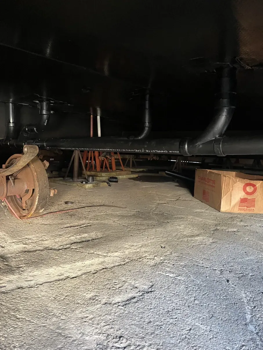 Under a large dark vehicle, showing a gravel floor and a cardboard box on the right
