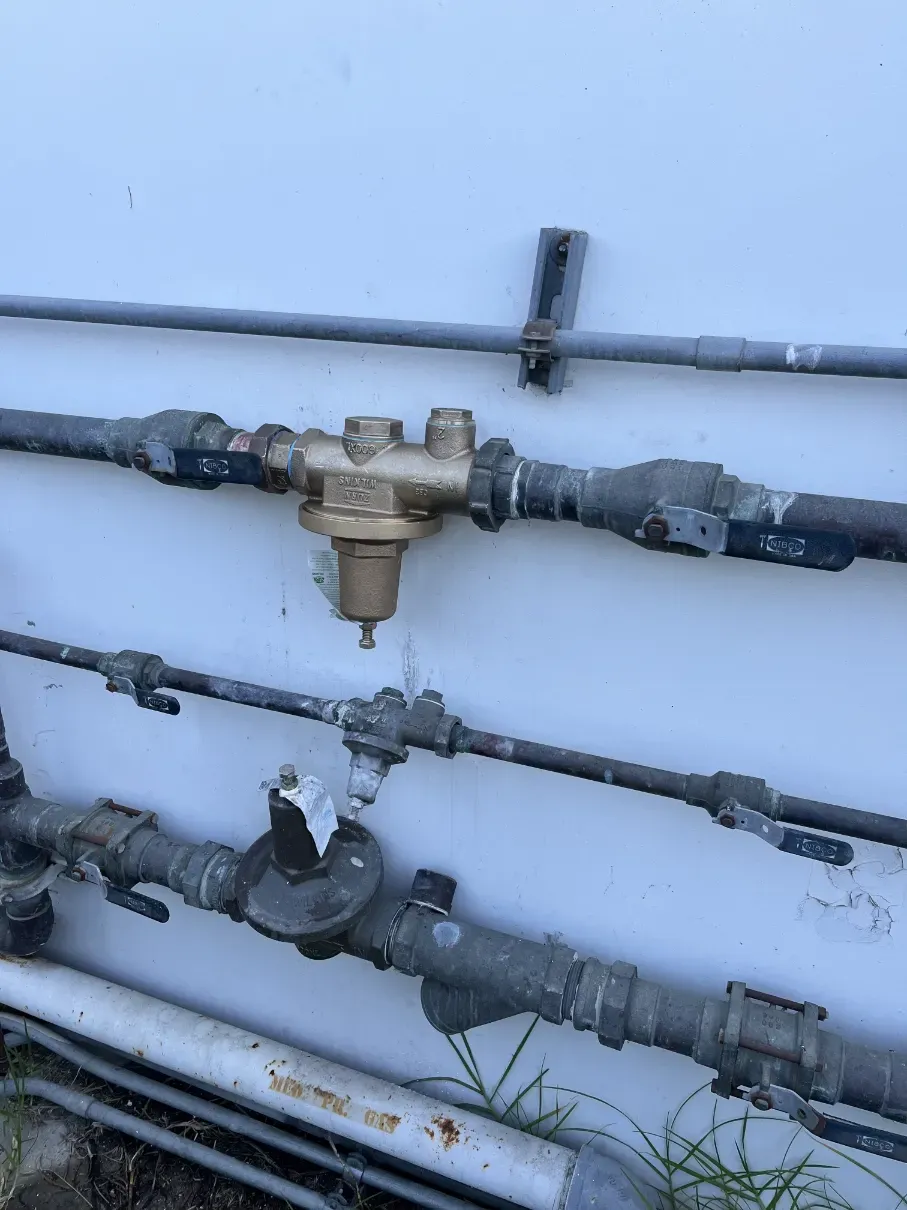Icy wall with exposed pipes and valves, including a central brass drain/filter assembly.