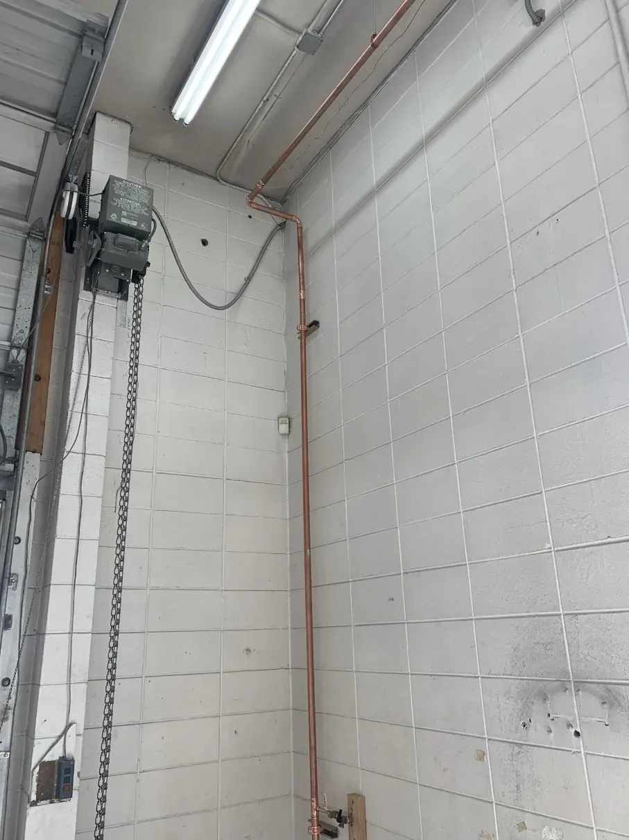Industrial interior with white brick walls, metal pipes, and a vertical chain hoist near the ceiling.