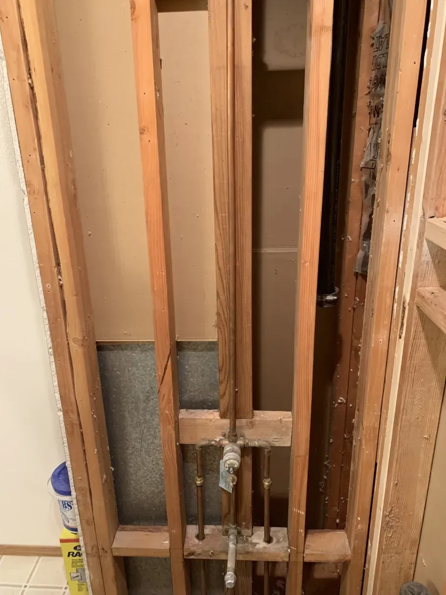 Open wall framing around exposed copper plumbing and a drain pipe.