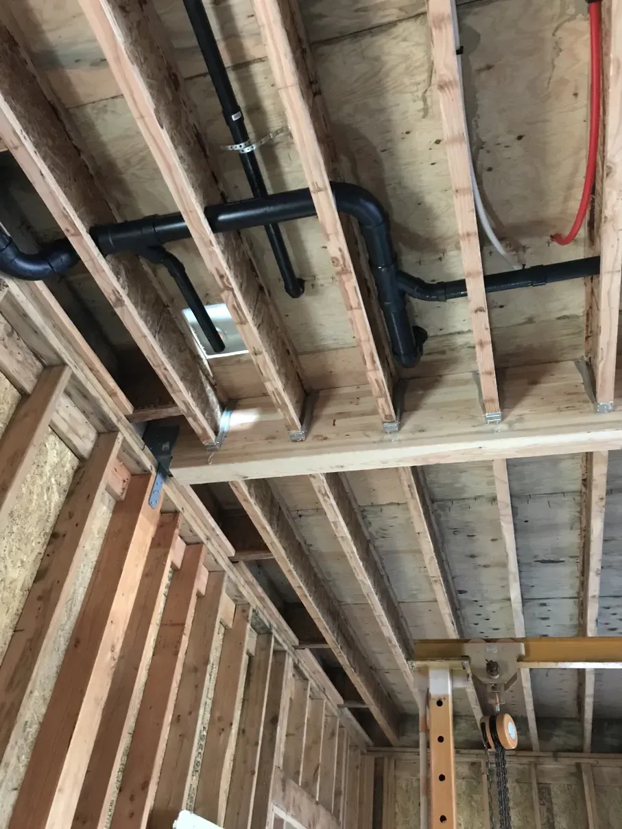 Unfinished room ceiling with exposed wooden joists, black pipes, and red wiring during construction