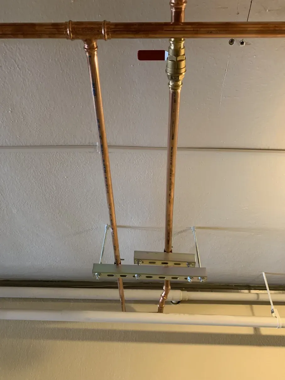 Copper pipes and valves on a ceiling, with a small green bracket and white conduit below.