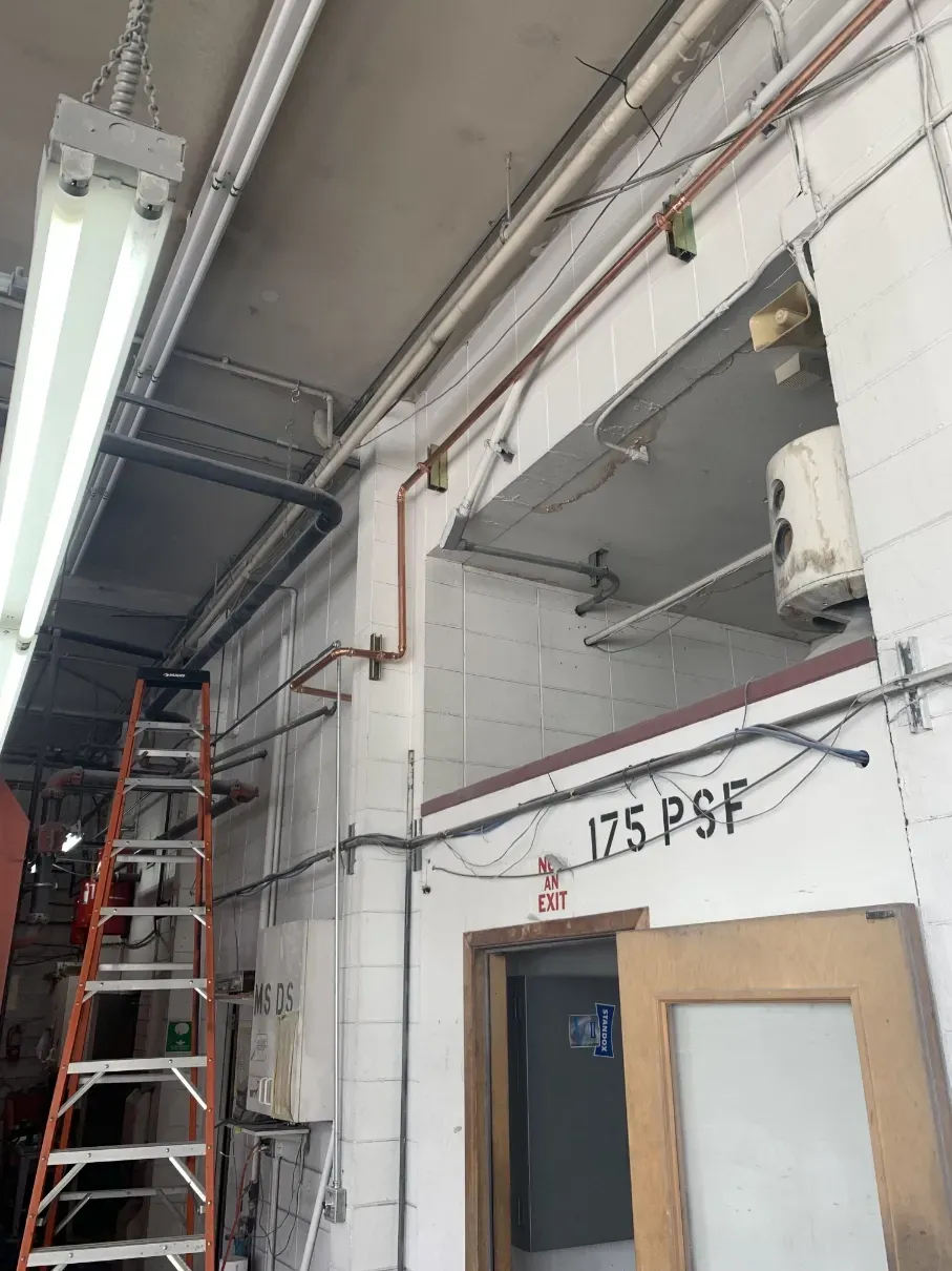 Interior hallway with a tall ladder, exposed ceiling pipes, and a doorway labeled “17.5 PSF”