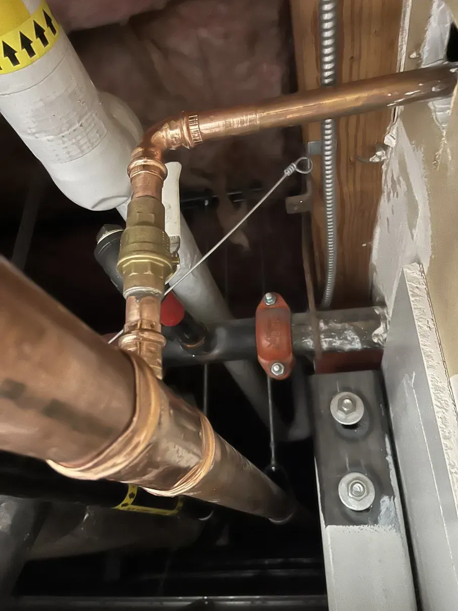 Copper pipes and a brass valve inside a wall cavity near HVAC equipment with a metal bracket.