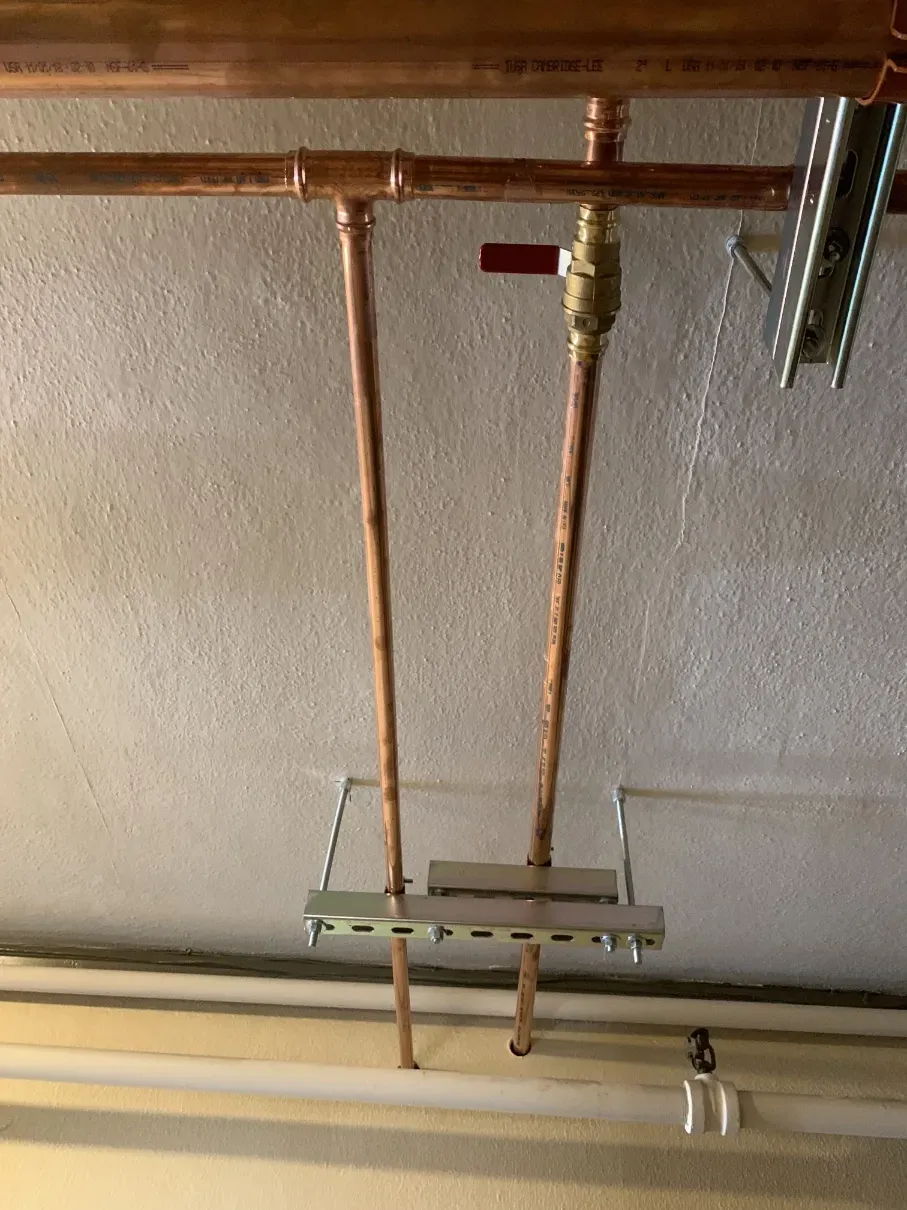 Copper pipes and a valve mounted on a basement ceiling beside a metal support bracket.
