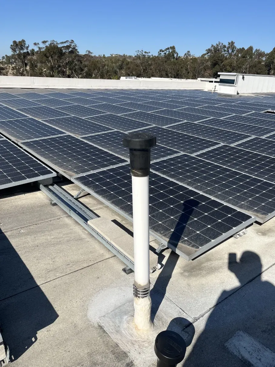 Rooftop solar panels under a blue sky, with a small vent pipe in the foreground.