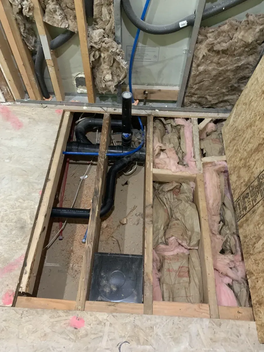 Exposed plumbing and wiring inside unfinished wall framing and floor joists during renovation.