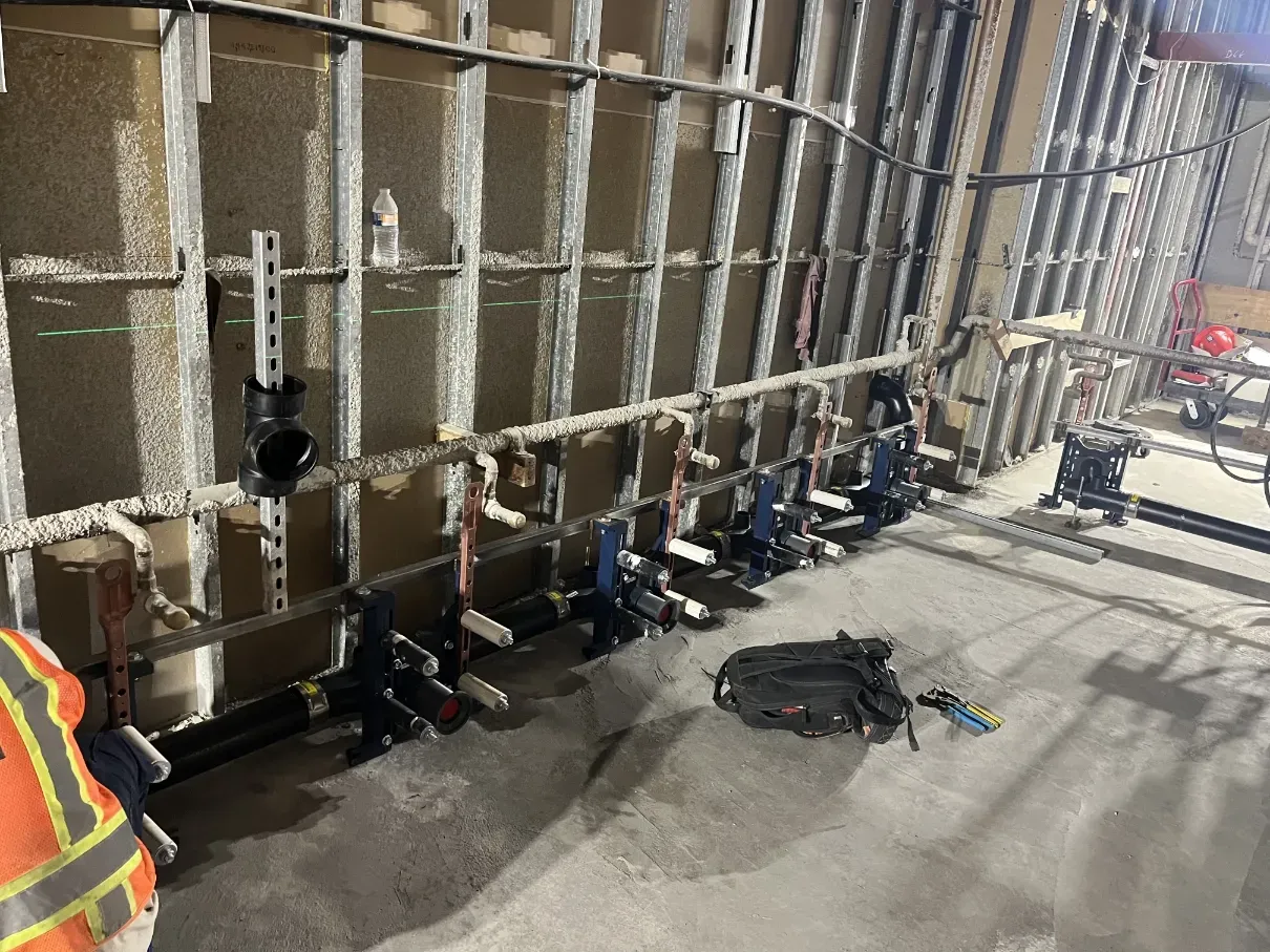 Construction site wall with a row of black pipe clamps and tools on the floor, next to a worker in a safety vest