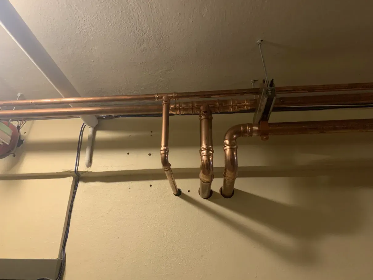 Copper pipes running along a ceiling, with several vertical pipe drops and fittings.
