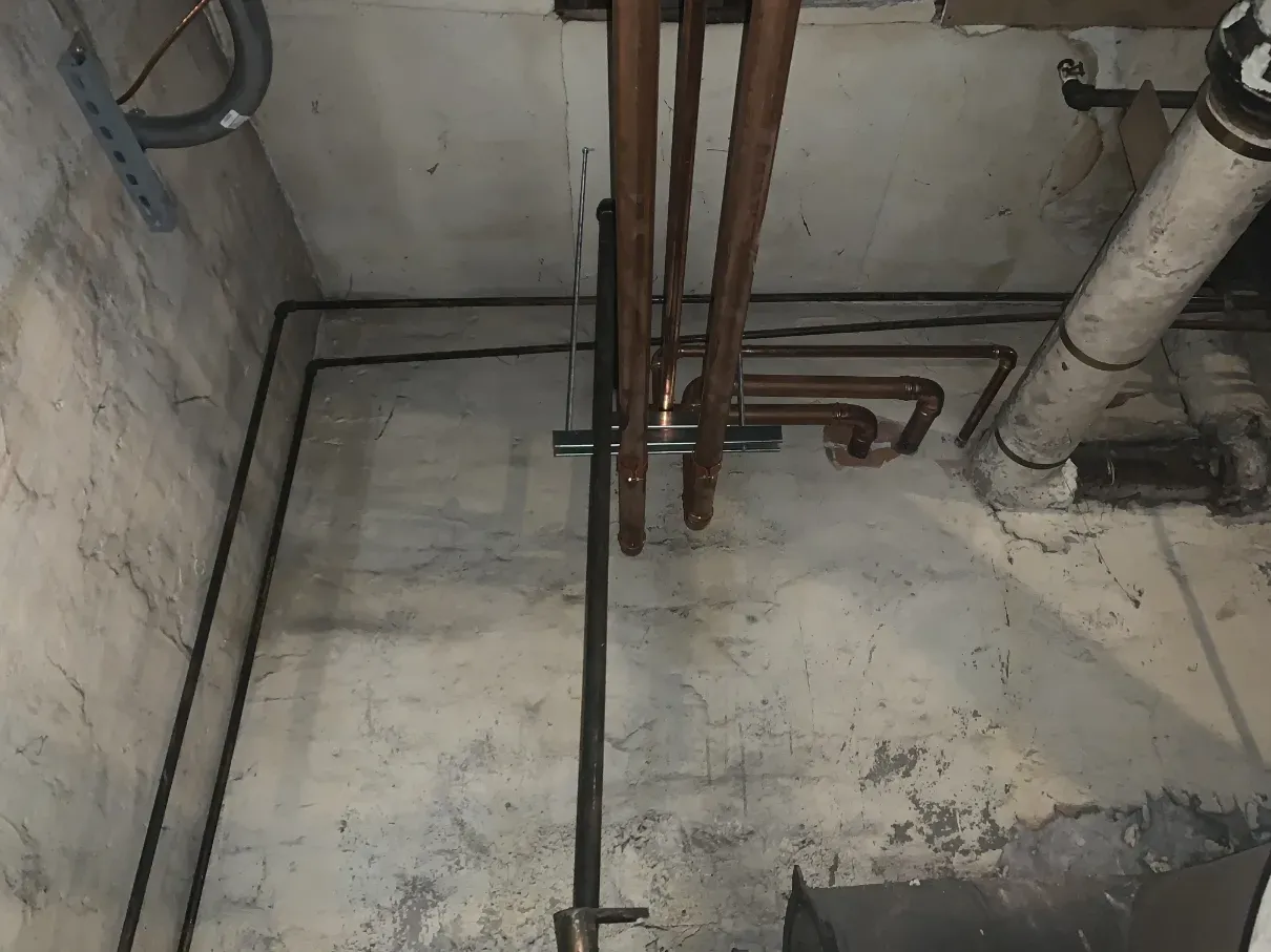 Concrete utility room with exposed pipes and cables along unfinished walls and floor
