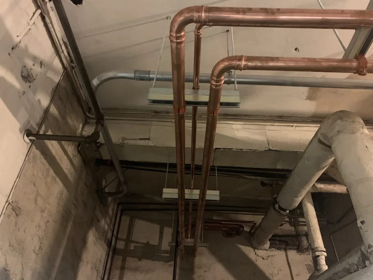Ceiling view of exposed copper and insulated pipes in an unfinished utility room