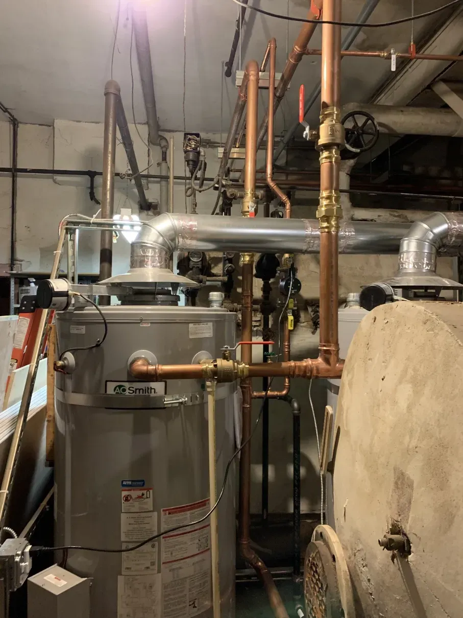 Mechanical room with metal pipes, ducts, and a large water heater beside an insulated tank.