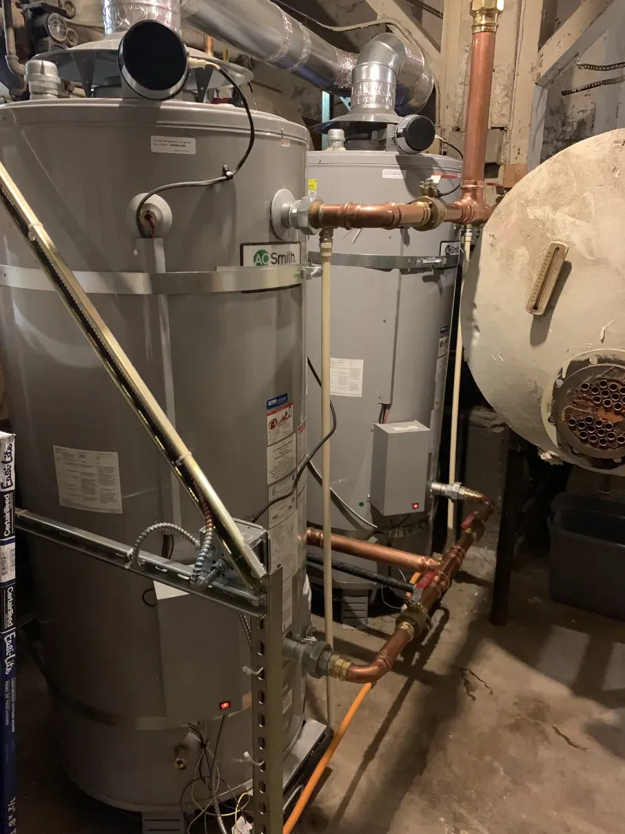 Basement utility room with large gray water heater, pipes, and a furnace or boiler unit