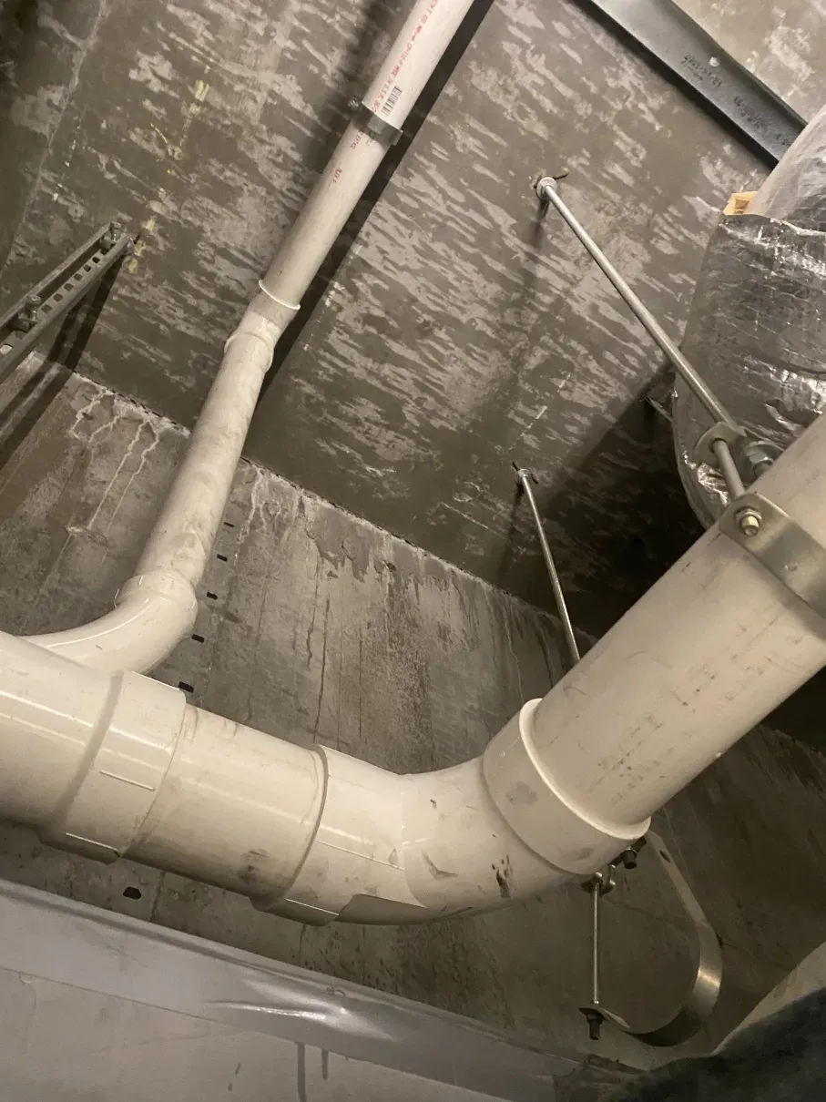 White PVC pipes crossing a damp concrete ceiling in an unfinished utility space