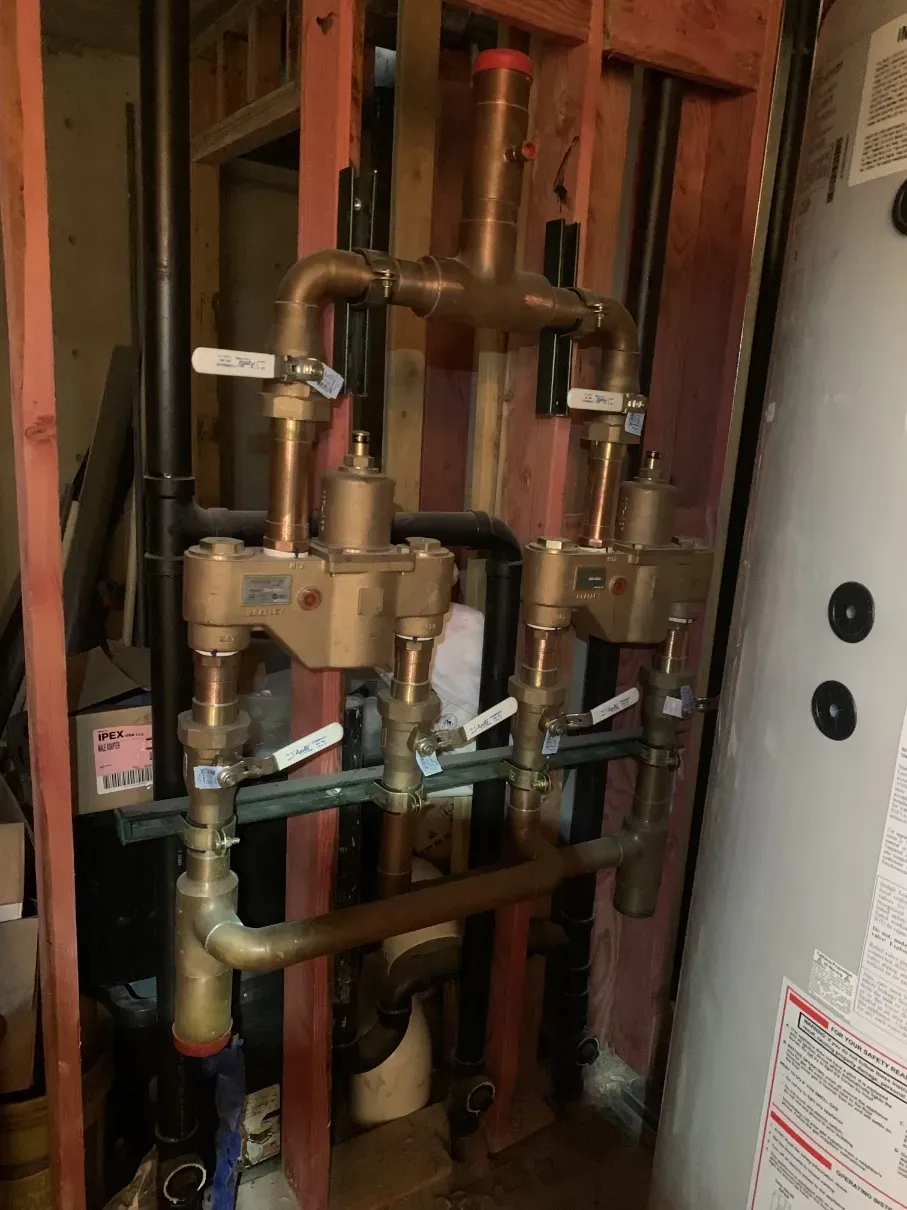 Copper and brass plumbing pipes and valves inside an open wall cavity, with labeled shutoff handles.