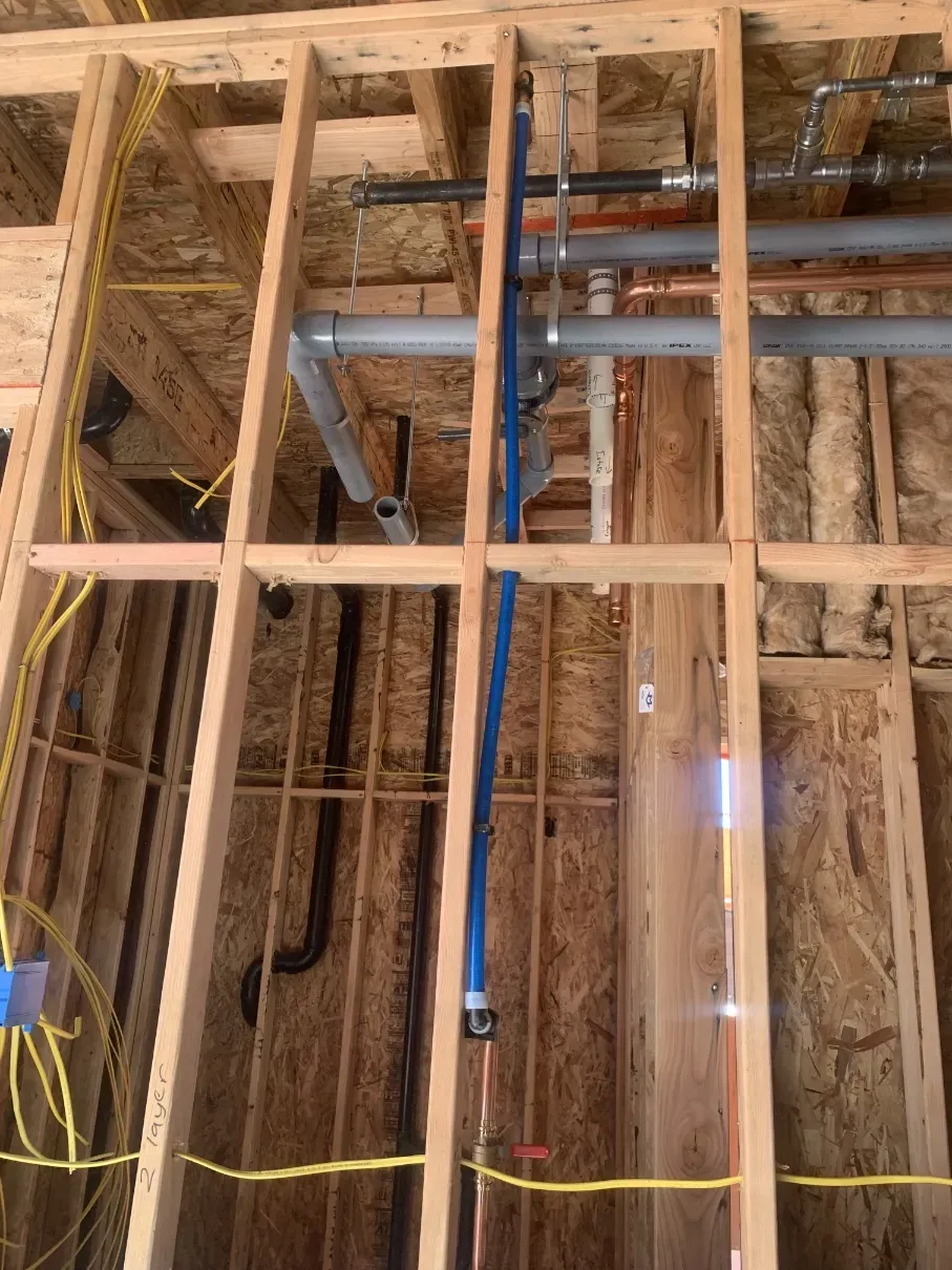 Exposed wooden wall framing with plumbing and electrical wiring in an unfinished construction space