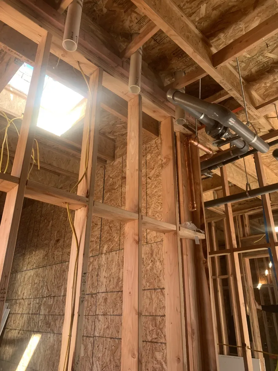 Exposed wooden framing and ceiling joists inside a building under construction, with a bright skylight opening.