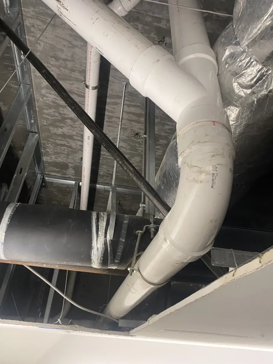 Industrial ceiling ductwork with white and black ventilation pipes in an unfinished space