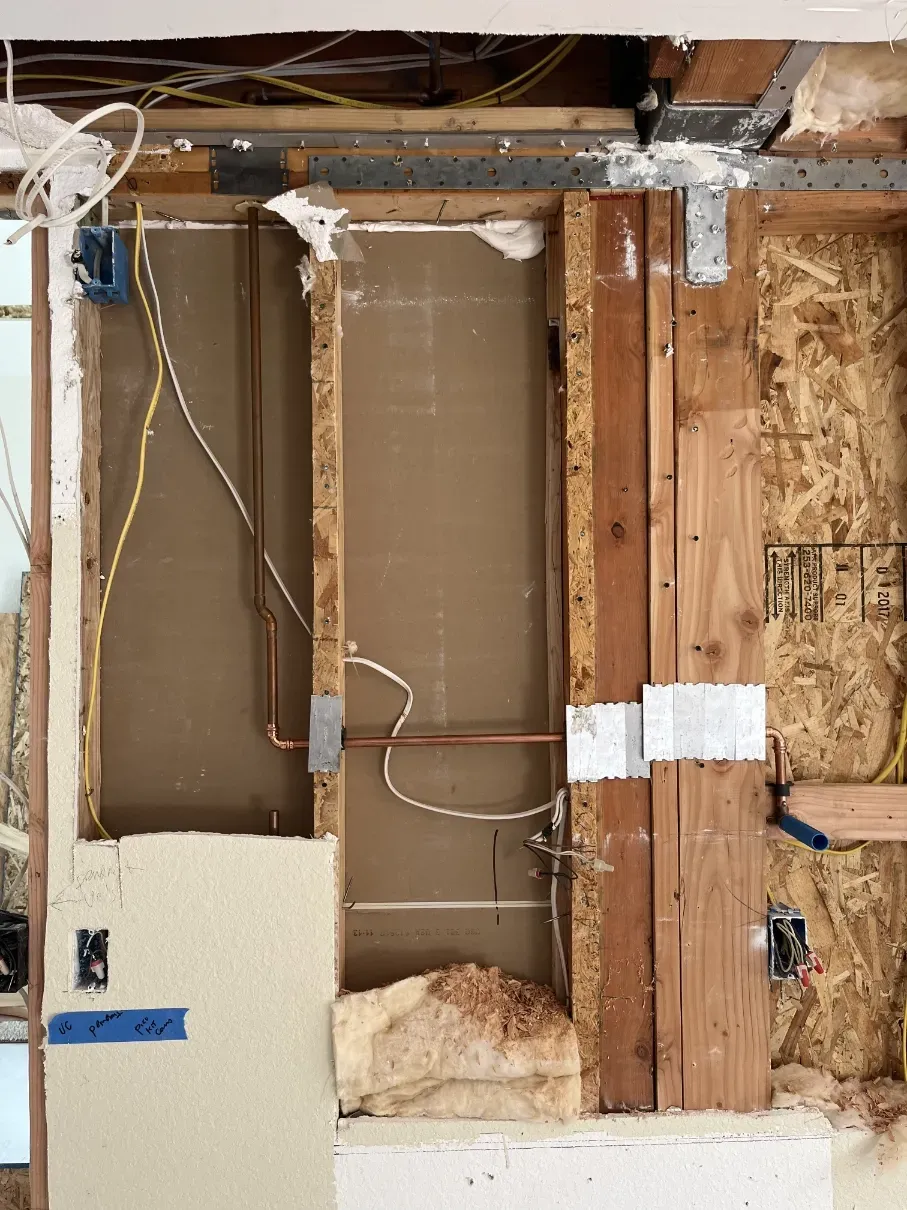 Partially demolished interior wall with exposed wiring, studs, insulation, and drywall patches