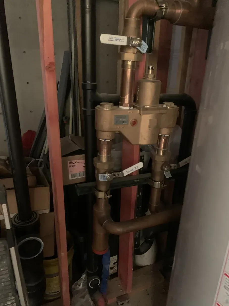 Copper plumbing pipes and valves in a utility closet, with a water meter and red shutoff handle.