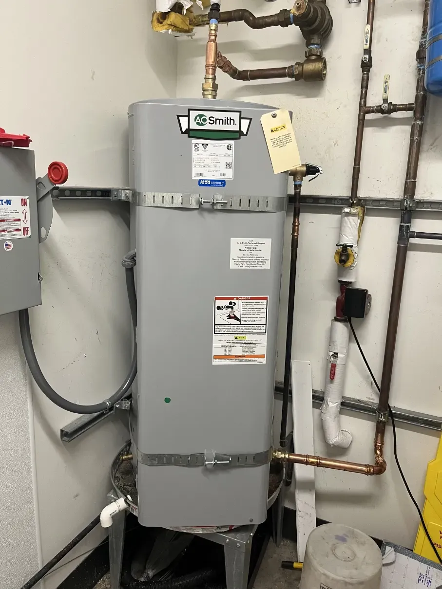 Gray water heater and plumbing pipes in a utility room, with gauges and valves attached.