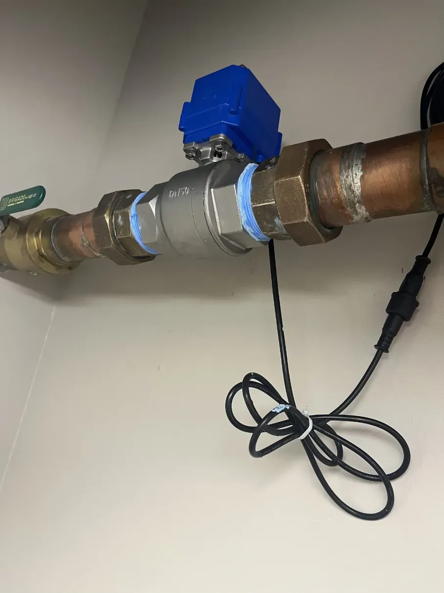 Blue valve on a copper pipe with a black cord hanging below, against a wall.