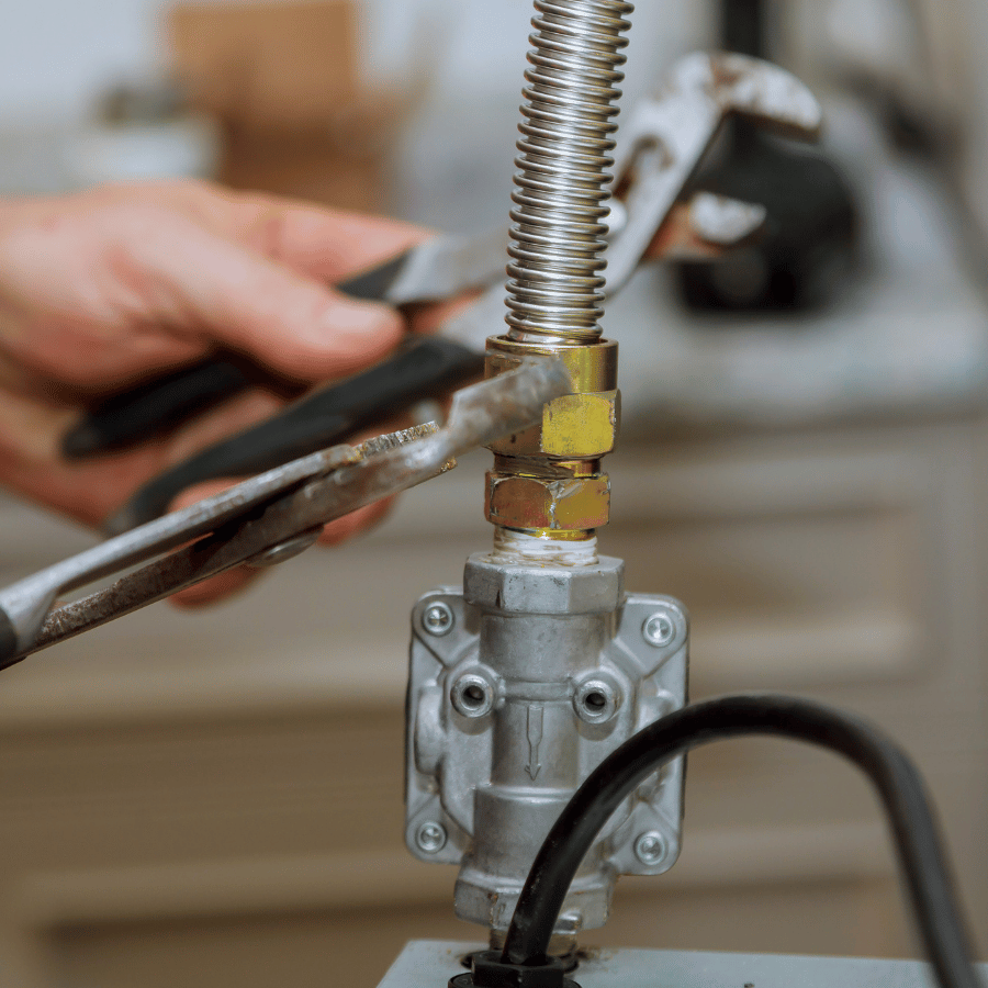 A hand uses pliers to tighten a metal gas pipe connection, ensuring a secure fit in a home appliance setup.