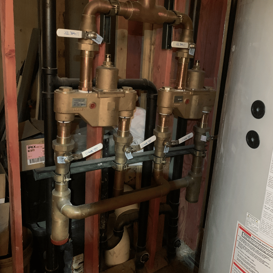 Copper plumbing valves and pipes in a utility room, with labeled handles, next to a large white water heater.