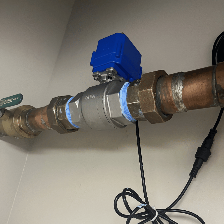 A blue motorized valve is connected to copper pipes on a wall, with visible wiring and a green lever for control.