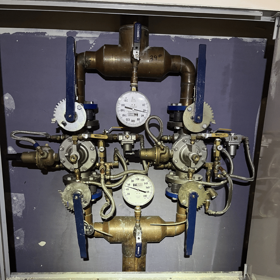 Complex plumbing system with gauges, valves, and pipes, displaying pressure readings in an industrial setting.
