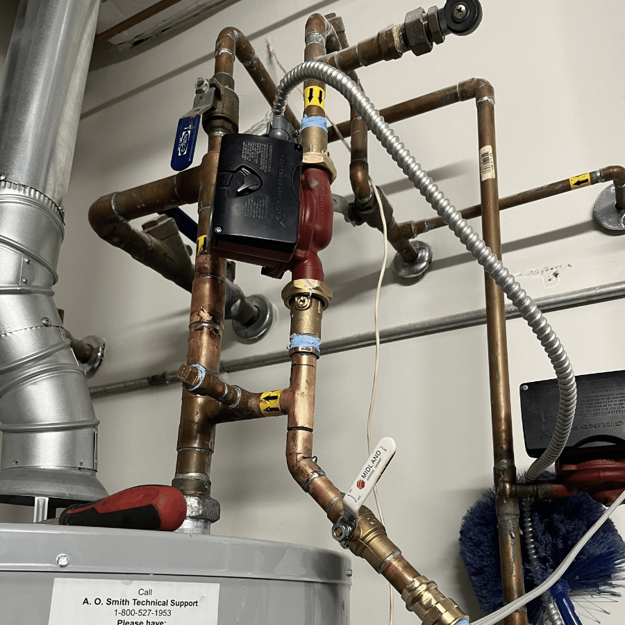 Industrial plumbing pipes and valves mounted above a metal tank in a utility room