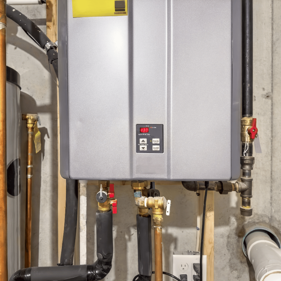 A tankless water heater mounted on a basement wall, displaying a digital temperature of 132°F, with visible pipes and valves.