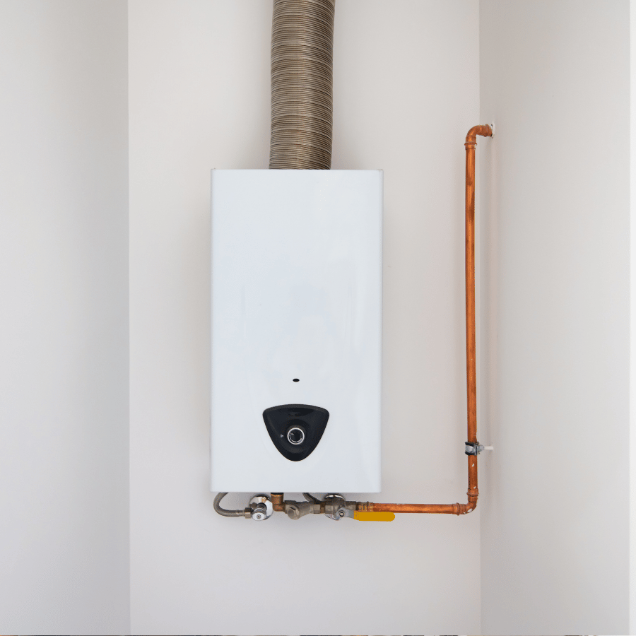 White tankless water heater with copper pipes and a vent, mounted on a wall in a corner, providing efficient home heating.