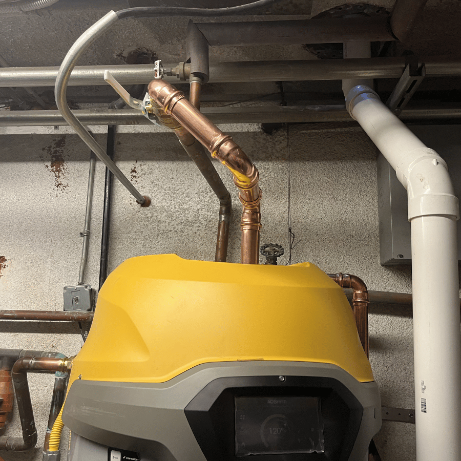 Basement with two AO Smith water heaters and copper pipes, surrounded by exposed walls and ductwork, creating an industrial feel.