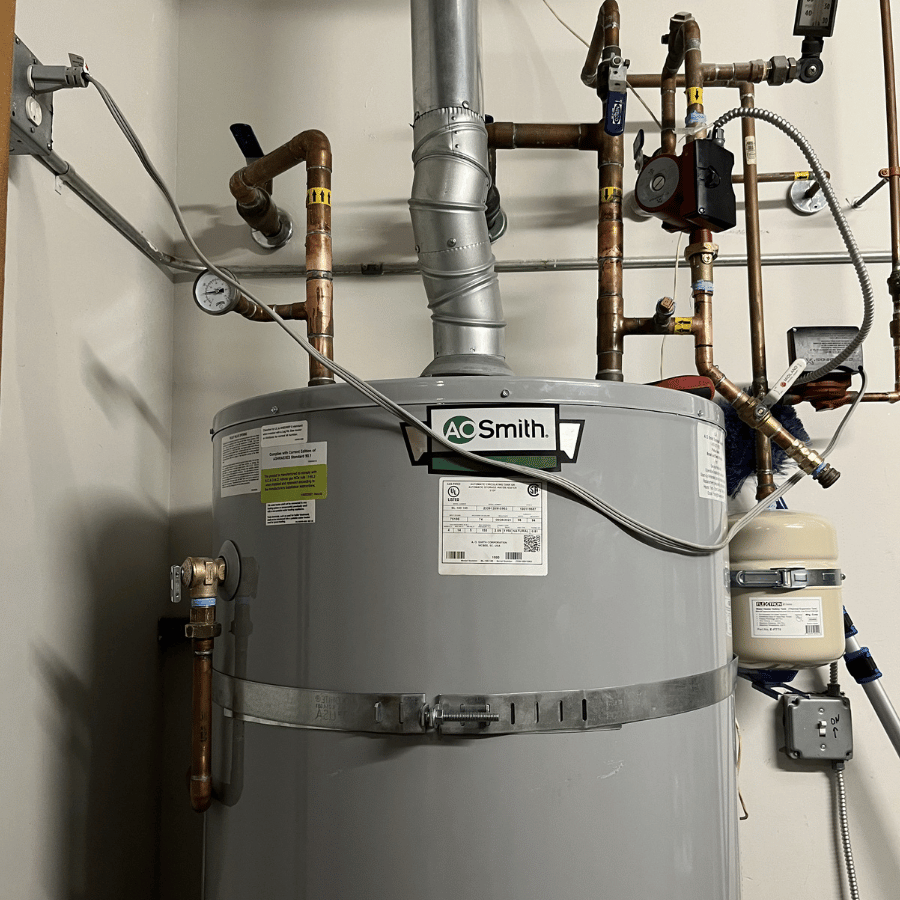 AO Smith water heater with pipes and gauges in a utility room, showcasing essential plumbing components and connections.