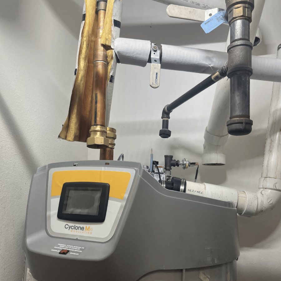 Yellow boiler with copper pipes in a basement setting, showcasing industrial plumbing and heating system components.