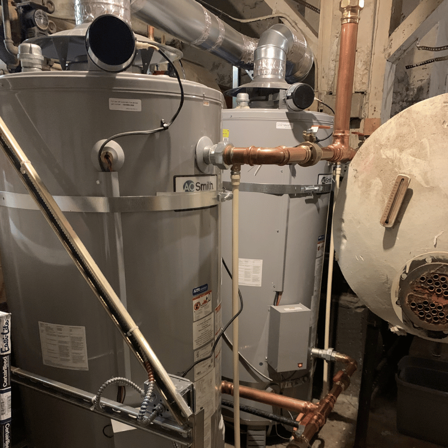 A Cyclone MX water heater with copper and PVC pipes in a utility room, showing its control panel and plumbing connections.