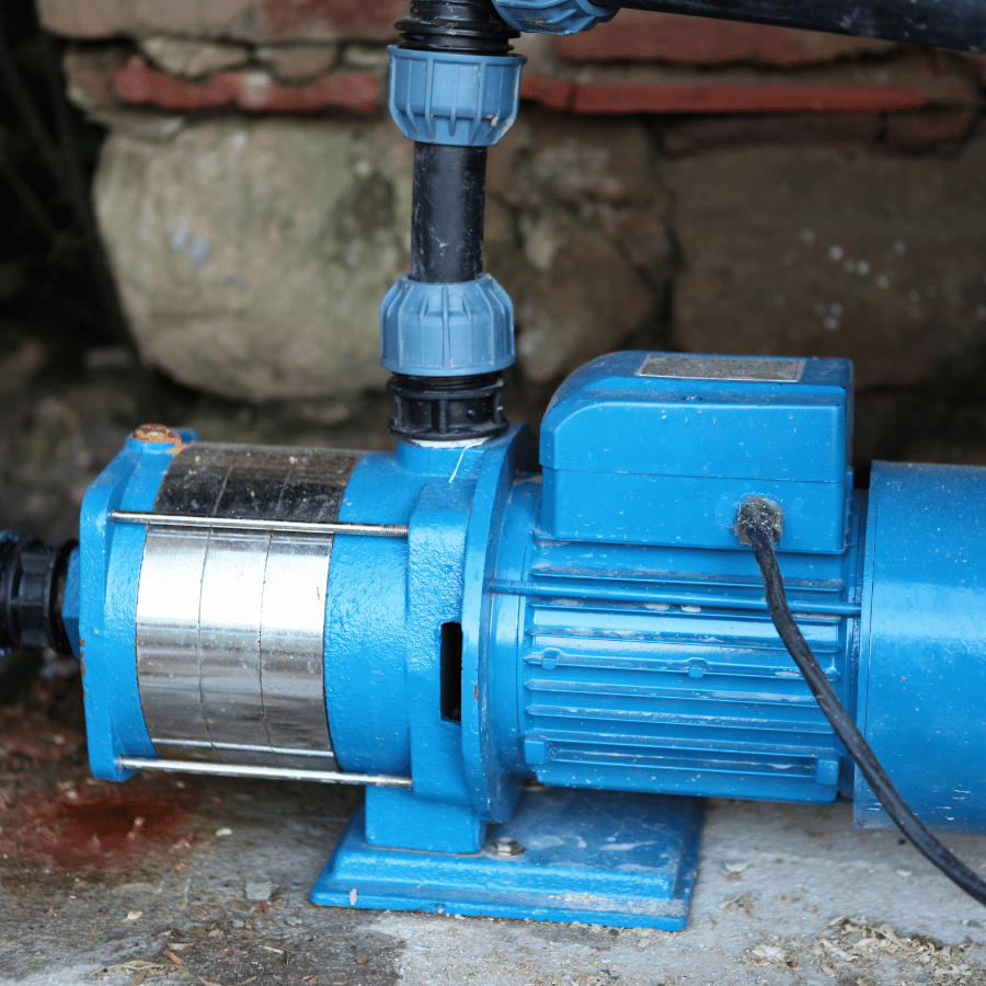 A blue water pump with a black pipe is mounted on a concrete surface, set against a stone wall background.