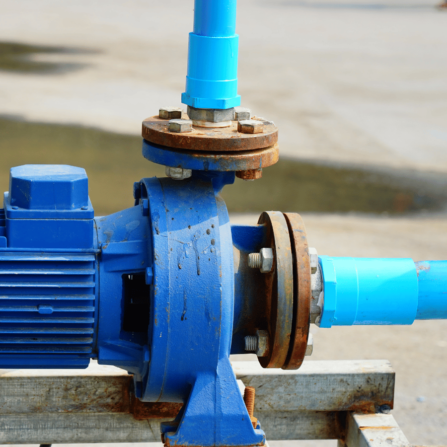Blue industrial pump with rusted bolts and pipes, set on a concrete surface, used for fluid transfer in industrial settings.