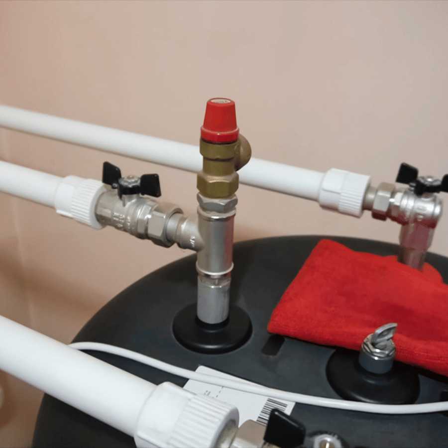 Pipes and valves on a water heater tank with a red safety cap and cloth, illustrating plumbing setup and maintenance essentials.